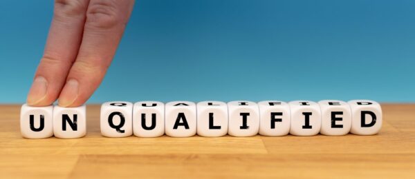 A persons hand on dice with the word un qualified kept on a wooden desk