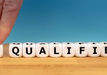 A persons hand on dice with the word un qualified kept on a wooden desk